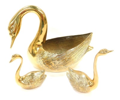 Three brass swan ornaments, comprising a large swan planter, with arch to neck, 25cm high, and two brass cygnet paperweights, 19cm high and 14cm high respectively. (3)