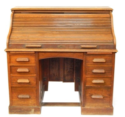 An Edwardian oak roll top writing desk, with S shape tambour opening to reveal a fitted interior, on pedestals of four drawers, 117cm high, 114cm wide, 65cm deep.