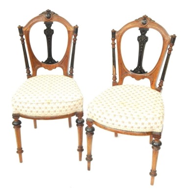 A pair of Edwardian walnut dining chairs, each with a carved and ebonised back, on floral padded set, on cabriole tapered legs.