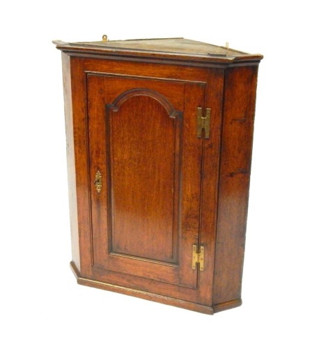 An 18thC oak hanging corner cupboard, with single trunk door with panel section, with brass hinges and escutcheon, 92cm high, 72cm wide, 50cm deep.