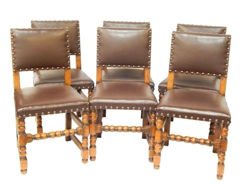 A set of six early 20thC Jacobean style oak dining chairs, each with a brown leather studded seat.