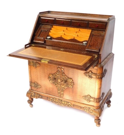 A 1930's carved oak bureau, with applied and carved detail, fitted interior, with single drawer above two cupboard base, on shell capped cabriole legs, 114cm high, 85cm wide, 46cm deep.