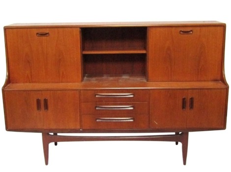 A mid century teak sideboard, with bookshelf top and cocktail cabinet, above two cupboard doors and three drawer central section, on shaped supports, 125cm high, 190cm wide, 50cm deep.