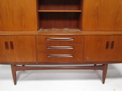 A mid century teak sideboard, with bookshelf top and cocktail cabinet, above two cupboard doors and three drawer central section, on shaped supports, 125cm high, 190cm wide, 50cm deep. - 2