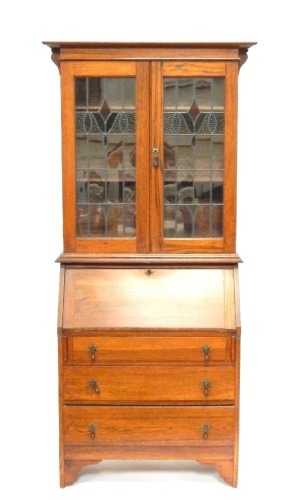 An Art Nouveau style oak bureau bookcase, the moulded cornice of two astragal and stained glass doors, with fall flap over three long drawers, on bracket feet, 191cm high, 90cm wide, 39cm deep.