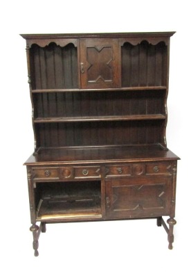 An early 20thC oak dresser, the plate rack top with two shelf section and single cupboard door, on moulded supports with sideboard base, with two drawers and two cupboard doors, 193cm high, 132cm wide, 50cm deep.