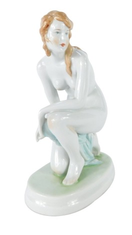 A 20thC Zsolnay Pecs porcelain figure, modeled as a naked kneeling woman, on an oval base, printed mark, 22cm high.