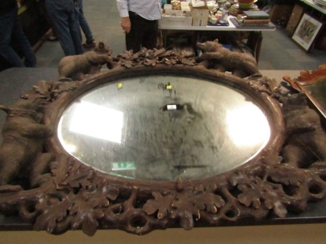 A 19thC wooden Black Forest oval wall mirror, the mirror plate in a carved frame of oak leaves, and four bears at intervals, 100cm high, 110cm wide. (AF)