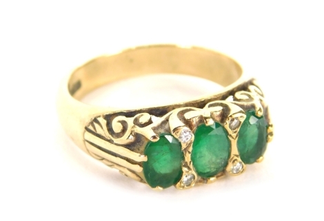 An emerald and diamond gypsy ring, set with four round brilliant cut tiny diamonds, and three oval emeralds, with scroll design setting, on a plain band, ring size O½, 5g all in.