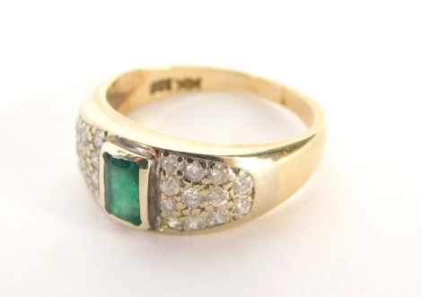 An emerald and diamond ring, the rectangular cut emerald in a rub over setting, with twenty four round brilliant cut tiny diamond set shoulders, totalling approximately 0.36cts and a central emerald weighing 0.50ct, on a yellow metal band stamped 14k, rin