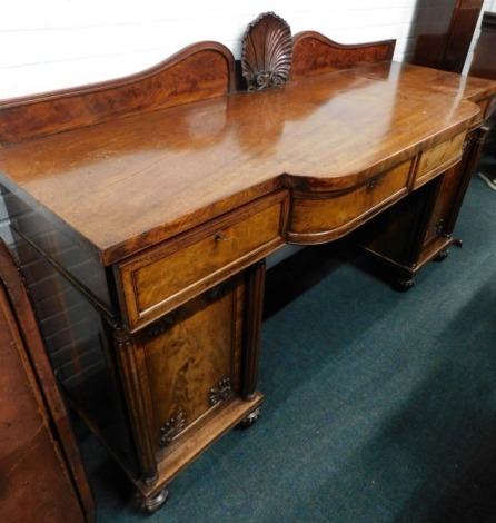 An early 19thC mahogany pedestal sideboard, the raised back decorated with a carved shell, the top with a bowed centre section above three drawers, the pedestals each with a frame veneered panelled door, embellished with acanthus carved spandrels flanked 