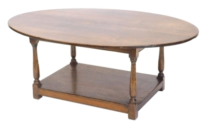 An oak coffee table, the oval top on turned supports with rectangular under tier, 47cm high, 123cm wide.