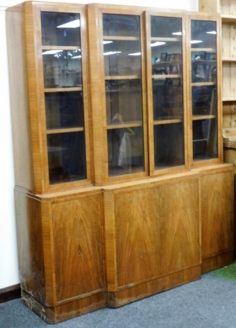 An Art Deco walnut breakfront bookcase, the top with four glazed doors, each enclosing three shelves, over four cupboard doors enclosing shelves, 176cm high, 152cm wide, 95cm deep.