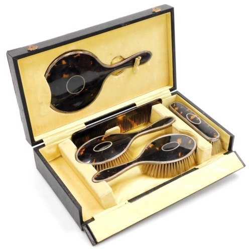 A George V silver and tortoiseshell backed toilet set, comprising pair of hair brushes, clothes brush, one further clothes brush lacking, hand mirror and a replacement none tortoiseshell comb, Birmingham 1922, in fitted box.