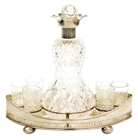 An Edward VII cut glass and silver liqueur set, the gourd shaped decanter with silver mount and cut glass topper, on an oval galleried tray, raised on bun feet, with matched Bohemian cut glass tops, John Grinsell & Sons, London 1903 and 1905, the tray 10½