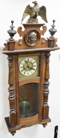 A late 19thC oak cased Vienna wall clock, the enamel style dial with Roman numerals, eight day movement, the case with eagles to crest, turned pilasters, with pendulum and key, 102cm high.