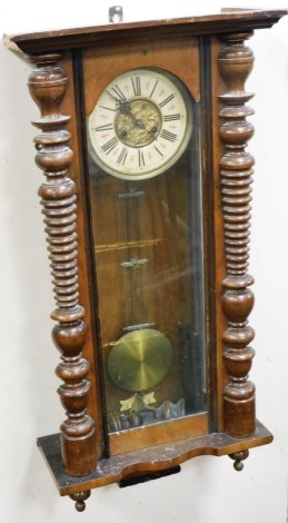 A late 19thC Continental walnut cased wall clock, circular brass dial with chapter ring bearing Roman numerals, eight day movement, the case with broken arch pediment and figural roundel, glass fronted with turned demi pilasters, with pendulum and key, 12