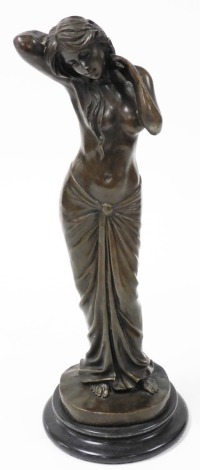 A bronze figure of a semi nude lady, modelled standing, stroking her hair, raised on a socle base, 41cm high.