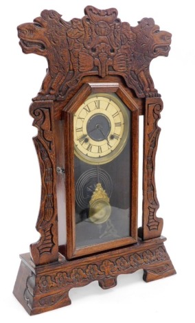 A late 19thC American oak cased mantel clock, gilt tin dial bearing Roman numerals, eight day movement with coil strike, the case with a glazed front, in a surrounding frame, carved with lions and flowers, raised on a base with bracket feet, with pendulum