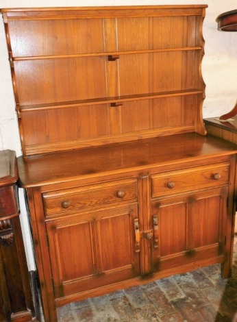 An Ercol elm dresser, with a two shelf waterfall plate rack, over a pair of doors above cupboard doors with sliding latch, raised on stile supports, 160cm high, 123cm wide, 47cm deep.