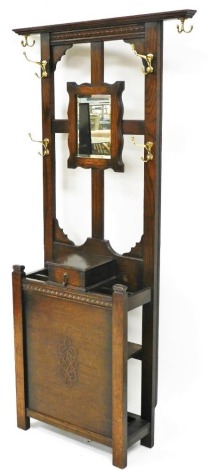 An early 20thC oak hall stand, with six coat hooks, a mirror back above a glove box and umbrella stand, raised on stile supports, 188cm high, 92cm wide.