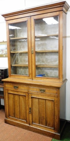 A Victorian oak cupboard bookcase, the out swept pediment over a pair of glazed doors enclosing three shelves, above two drawers over two panelled doors enclosing a single shelf, raised on a plinth base, 229.5cm high, 130cm wide, 53cm deep.