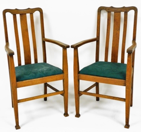 A pair of Arts and Crafts oak carved elbow chairs, with drop in seats, raised on tapering square legs.