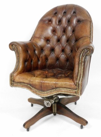 An early 20thC brown leather swivel armchair, with button back and seat.