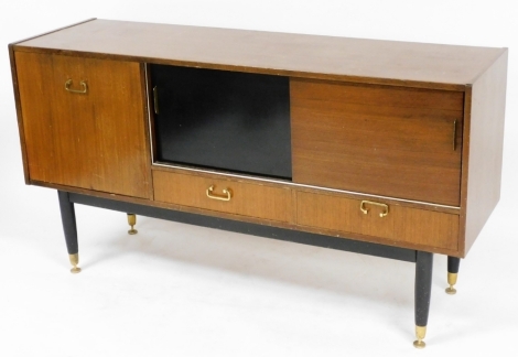 A 1950's G-Plan teak sideboard, with a drop down drinks cabinet, flanked to the right by two sliding doors, one ebonised, over two frieze drawers, raised on turned ebonised legs, brass capped on brass feet, circa 1960, 77cm high, 143cm wide, 43cm deep. 