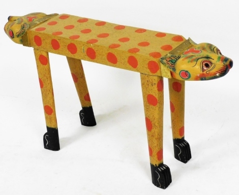 A Balinese painted wooden cat stool, with double headed ends, the body painted with red spots, raised on four feet, 51.5cm high, 101.5cm wide.