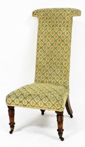 A Victorian mahogany prie dieu chair, upholstered in repeating rose patterned fabric, raised on lappet carved and turned legs, brass capped on castors.