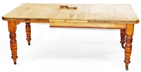 A Victorian pine wind out dining table, with one additional leaf, raised on turned legs, brass capped on castors, 72cm high, 178cm wide extended, 107cm deep.