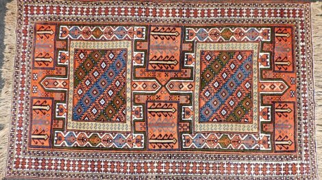 A Persian Kurdish red ground rug, with four central rectangular fields, containing geometric motifs and stylised trees, against a floral ground, within repeating geometric borders, 196cm x 117cm.