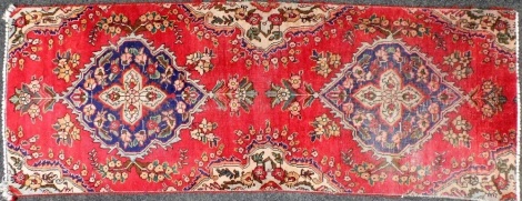 A Keshan red ground runner, with two central blue medallions decorated with flowers, against a floral decorated ground, 198cm x 74cm. (AF)