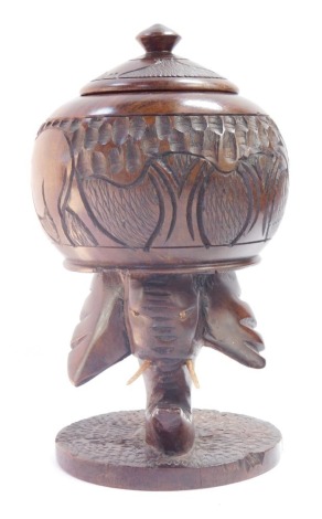 An African early 20thC lignum vitae box and cover, carved with animals, raised on an elephant's head support and a circular base, 23cm high.