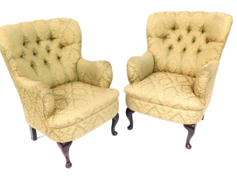 A pair of green button back armchairs, each with a button back and shaped arms with a green and gold scroll fabric, on stained mahogany legs, 92cm high, 60cm wide, 52cm deep.