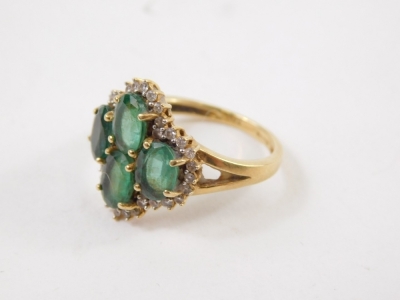 An 18ct gold dress ring, claw set with four central green stones surrounded by small diamonds on a part pierced shank, size N-O, 4.8g all in. - 2