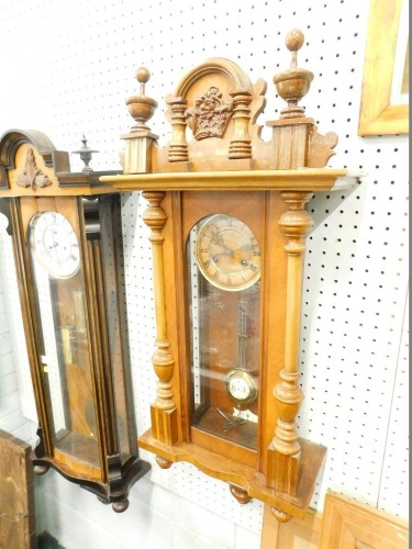 An early 20thC walnut Vienna style wall clock, the 13cm diameter Roman numeric dial help in a three part glazed case surmounted by finials and centred by raised crown, with serpentine front, eight day movement, pendulum and key, 83cm high.