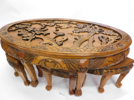 An oriental hardwood oval coffee table, carved with birds, figures, trees, etc. in relief, on cabriole legs with paw feet, sold with a matching set of six nesting tables, the top 120cm x 74cm.