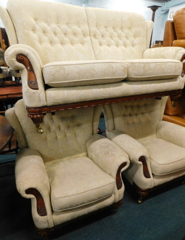 A walnut three piece suite, comprising two-seater sofa, and two armchairs, upholstered in gold pattern fabric with show frame on low with button feat, with brass castors, 88cm wide. The upholstery in this lot does not comply with the 1988 (Fire & Fire Fur