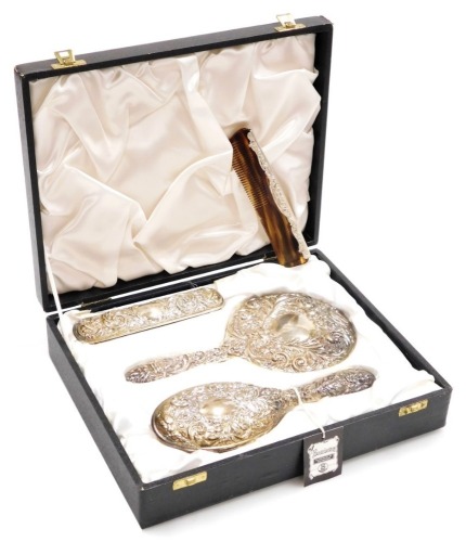 An Elizabeth II silver mounted four piece dressing table set, comprising hand mirror, hairbrush, clothes brush and comb, each heavily repousse decorated with leaves, flowers, scrolls, vacant cartouche and mask, Birmingham 1976, in fitted case.