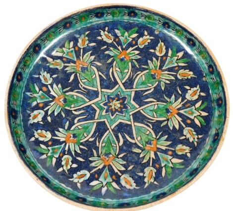 An early 20thC Iznik pottery dish, decorated with flowers and scrolling leaves against a blue ground, 24.5cm wide.