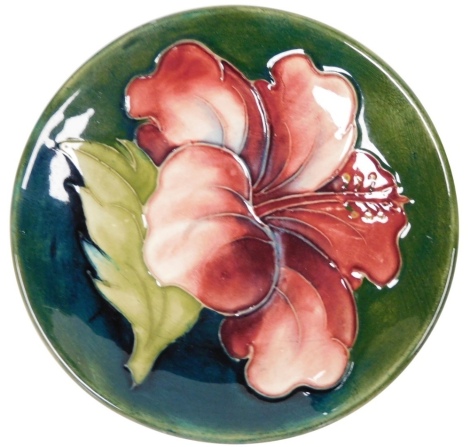 A Moorcroft pottery pin dish, decorated in the Hibiscus pattern, against a blue to green ground, impress marks, 11.5cm diameter.