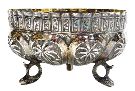 An Indian white metal bowl, heavily decorated with repeat motifs, palm trees and animals, raised on three fish shaped supports, 2.46oz, 5cm high, 8.5cm diameter.