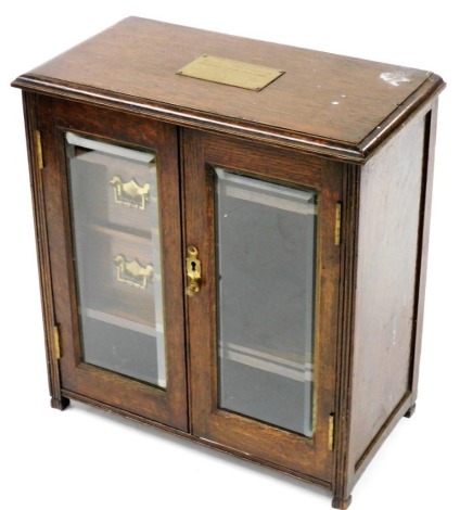 An early 20thC oak smoker's cabinet, the two hinged glass fronted doors enclosing a fitted interior with one long and two short drawers, with two recesses, 36cm high, 34cm wide, 17cm deep.