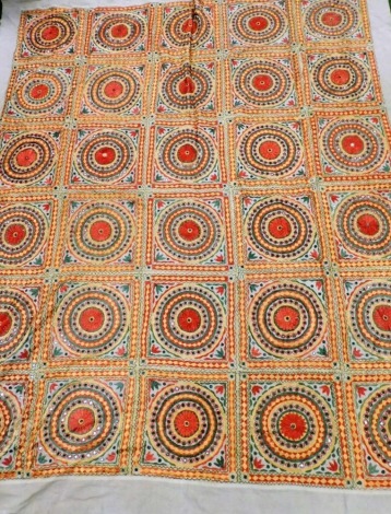 An Eastern embroidered double bedspread, in red orange and green with mirrored embellishment, against a fawn coloured material, 252cm x 212cm.