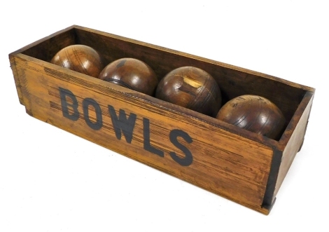 Four Lignum vitae bowls, contained in pine open box painted to the front with 'bowls', 42cm wide.