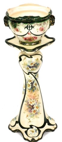 An early 20thC pottery jardiniere on stand, printed with cabbage roses and meadow flowers against a green and white ground, gilt heightened, 84cm high. (AF)