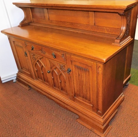 A Continental Gothic oak style sideboard, with a panelled back over a carved frieze drawer above a pair of carved doors, opening to reveal a single shelf, flanked by a pair of linen fold panel doors, raised on ogee bracket feet, 130cm high, 179cm wide, 54