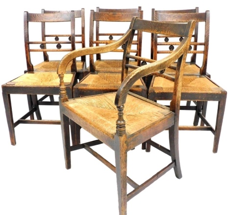 A set of seven 19thC country made elm dining chairs, each with a bar back inset with roundels, a rush seat on square tapering legs, one with arms.